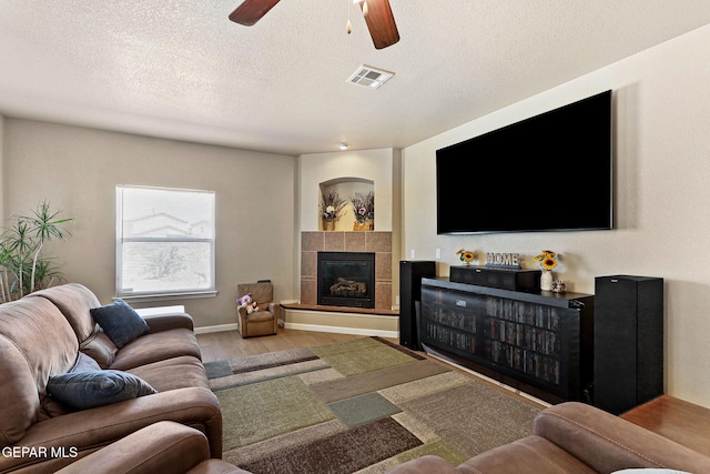 living room featuring a ceiling fan, wood finished floors, visible vents, a textured ceiling, and a tiled fireplace