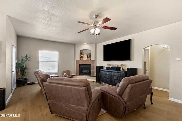 living room with a ceiling fan, arched walkways, wood-type flooring, a textured ceiling, and a tiled fireplace