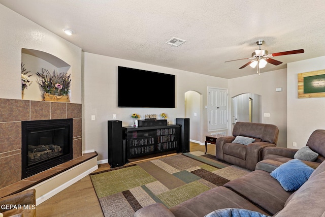 living room with visible vents, a textured ceiling, wood finished floors, arched walkways, and a fireplace