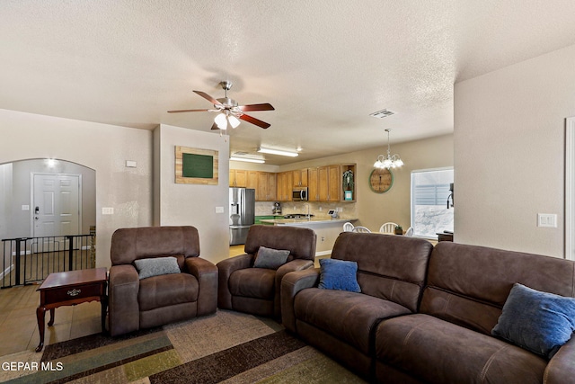 living area featuring arched walkways, visible vents, ceiling fan with notable chandelier, and a textured ceiling