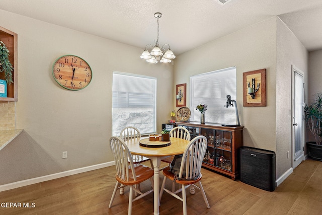 dining space featuring baseboards, light wood-style flooring, a textured wall, a notable chandelier, and a textured ceiling