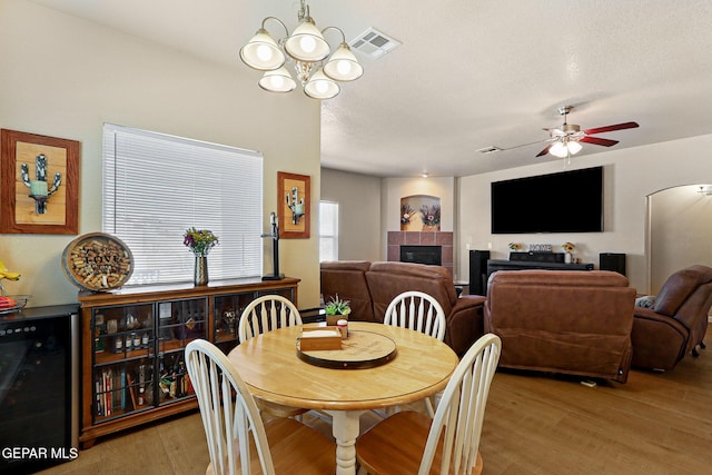 dining space with light wood-type flooring, visible vents, beverage cooler, a textured ceiling, and a fireplace