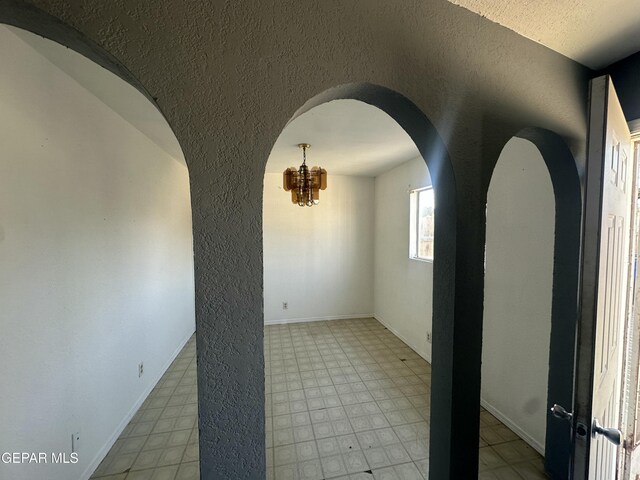 empty room featuring tile patterned floors, arched walkways, an inviting chandelier, baseboards, and a textured wall