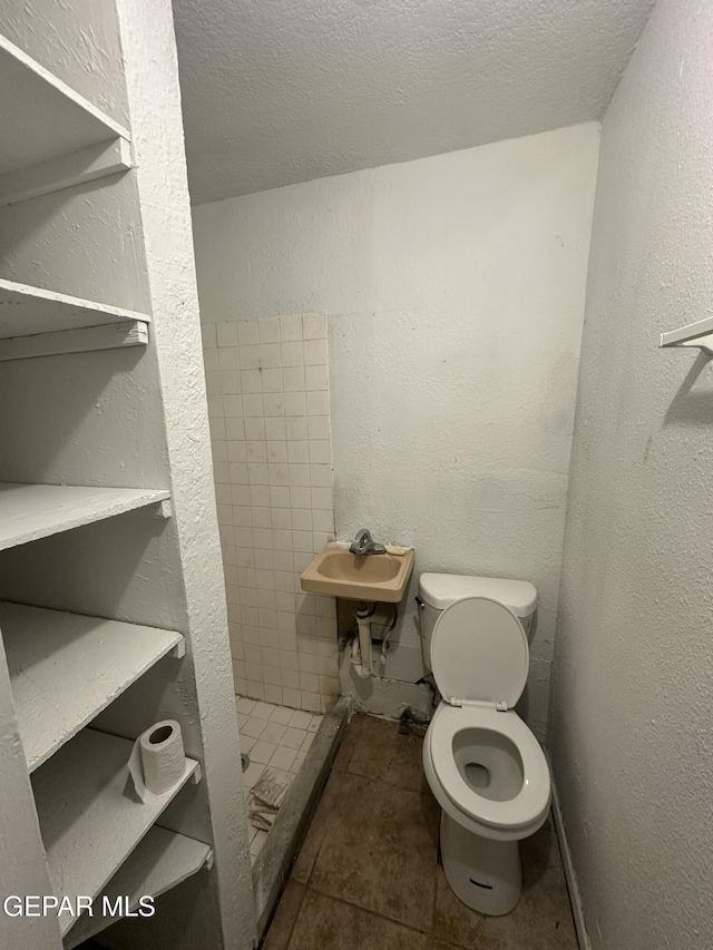 full bath with toilet, a stall shower, a textured wall, a textured ceiling, and a sink