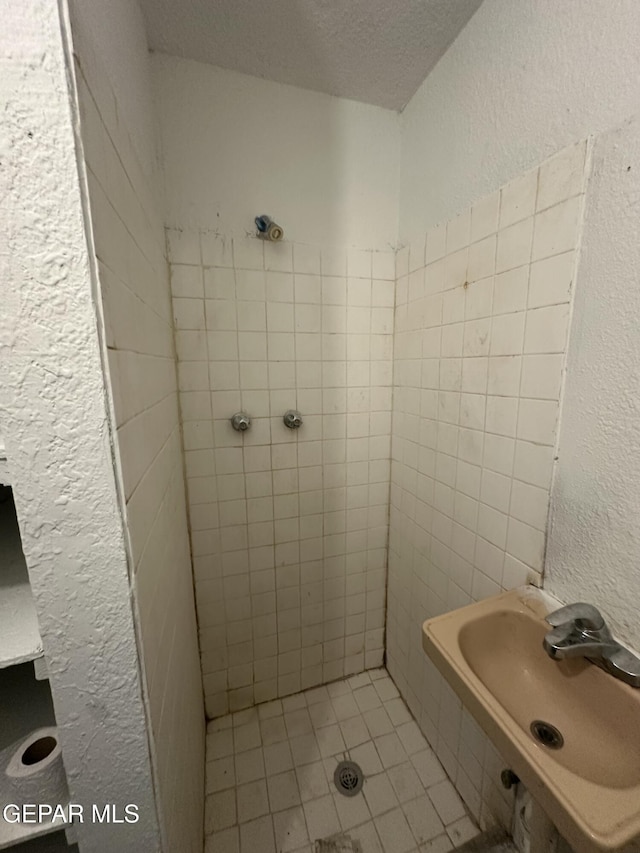 bathroom featuring a sink, a textured ceiling, a shower stall, and a textured wall