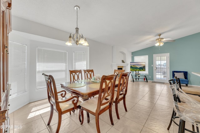 dining room with ceiling fan with notable chandelier, vaulted ceiling, light tile patterned flooring, and a fireplace