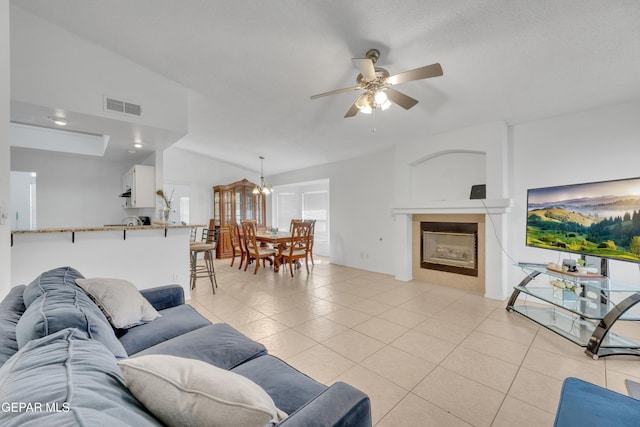 living area featuring visible vents, a tiled fireplace, lofted ceiling, light tile patterned floors, and ceiling fan with notable chandelier