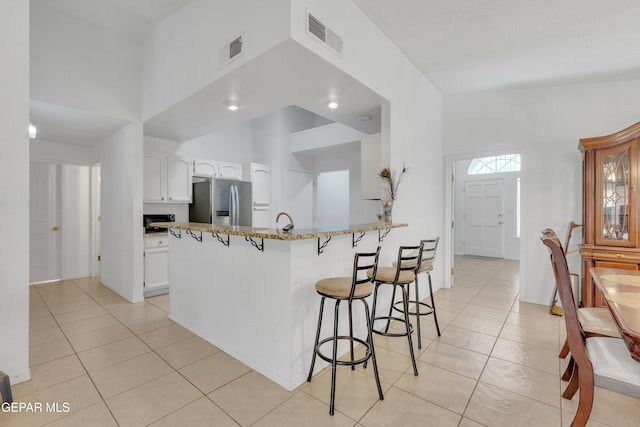 kitchen with white cabinetry, a breakfast bar area, stainless steel fridge with ice dispenser, and visible vents