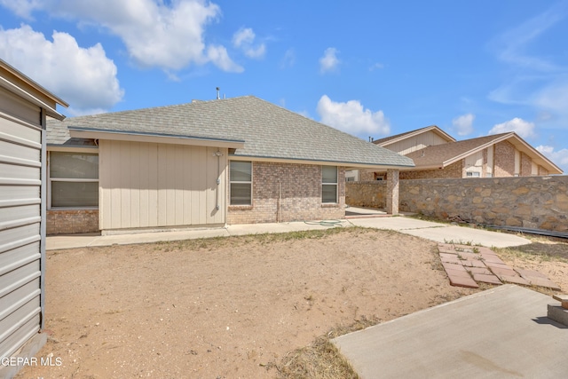 back of property with a patio area, a shingled roof, brick siding, and fence