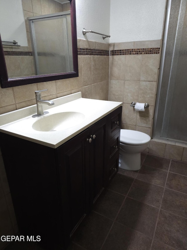 bathroom featuring toilet, a stall shower, vanity, and tile walls