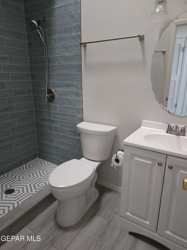 bathroom featuring wood tiled floor, tiled shower, toilet, and vanity