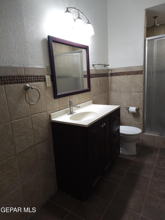 full bath with tile patterned floors, toilet, a stall shower, tile walls, and vanity