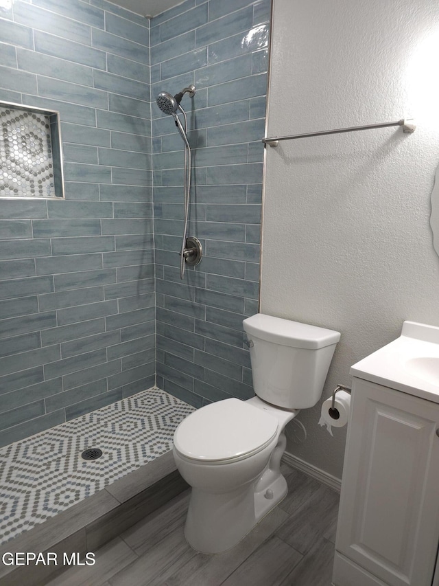 bathroom with baseboards, toilet, a tile shower, wood finished floors, and vanity