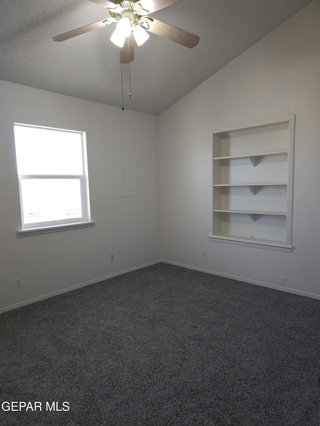 empty room featuring vaulted ceiling, built in shelves, dark colored carpet, and a textured ceiling