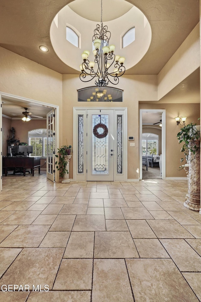 foyer entrance featuring light tile patterned floors, ceiling fan with notable chandelier, baseboards, and a towering ceiling