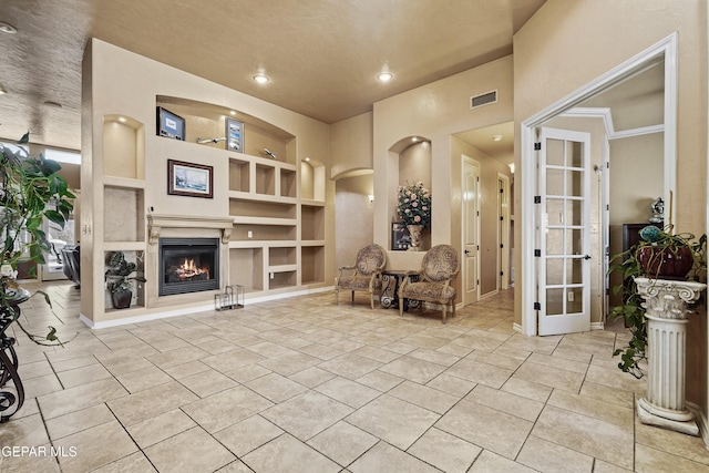 sitting room featuring visible vents, built in features, arched walkways, light tile patterned flooring, and a glass covered fireplace