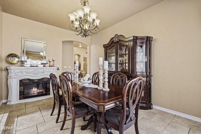 dining space featuring baseboards, light tile patterned flooring, arched walkways, a glass covered fireplace, and a notable chandelier