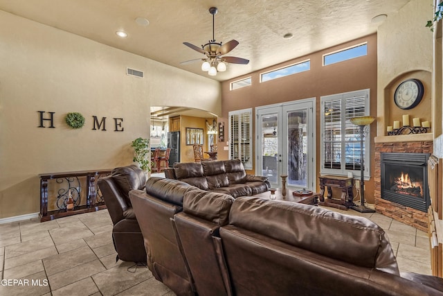 living room featuring visible vents, a fireplace, a high ceiling, arched walkways, and a ceiling fan