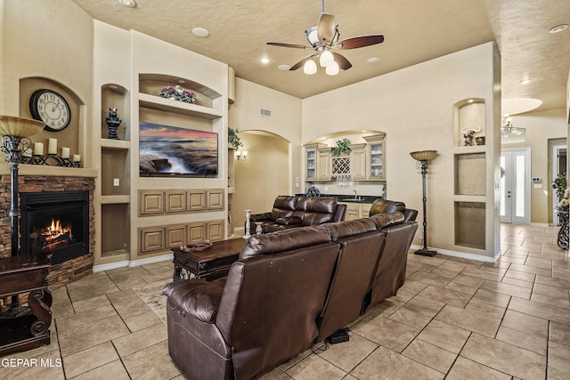 living room with visible vents, built in shelves, a stone fireplace, baseboards, and ceiling fan