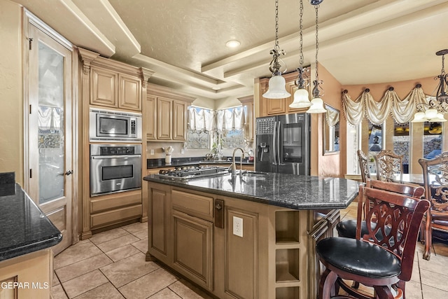 kitchen with a center island with sink, dark stone countertops, appliances with stainless steel finishes, hanging light fixtures, and a sink