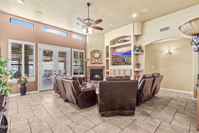 living area featuring visible vents, built in shelves, a ceiling fan, a textured ceiling, and a brick fireplace