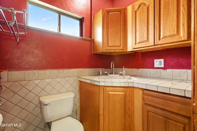 bathroom featuring tile walls, toilet, vanity, and a textured wall