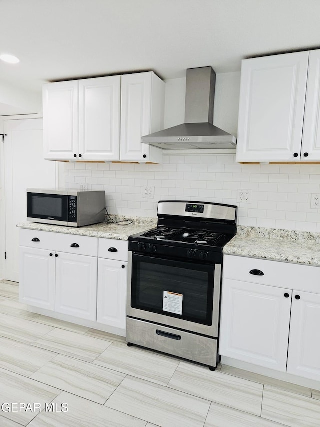 kitchen featuring backsplash, white cabinetry, stainless steel appliances, and wall chimney range hood