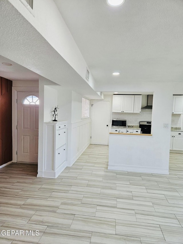 kitchen featuring stainless steel microwave, tasteful backsplash, white cabinetry, wall chimney exhaust hood, and range