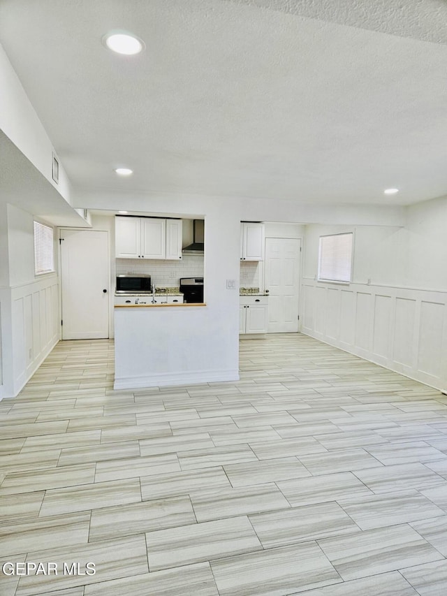 kitchen with stove, stainless steel microwave, white cabinetry, and wall chimney range hood