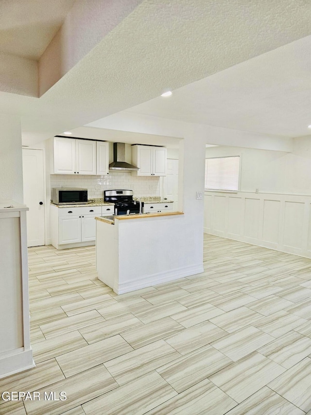 kitchen with light countertops, appliances with stainless steel finishes, white cabinetry, wall chimney range hood, and tasteful backsplash