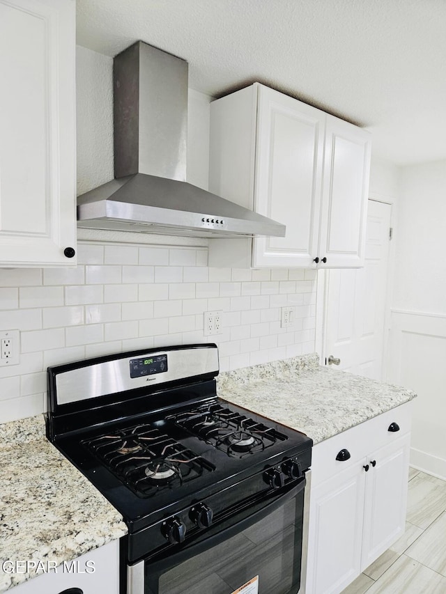 kitchen with light stone counters, gas range, white cabinetry, and wall chimney exhaust hood