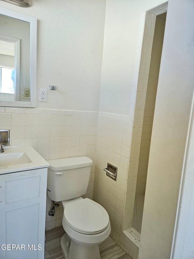 bathroom featuring vanity, toilet, tile walls, and a shower stall