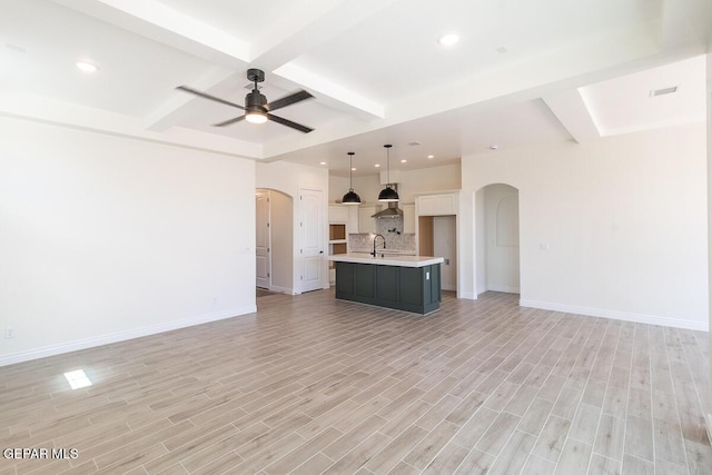 unfurnished living room with a sink, beamed ceiling, arched walkways, and light wood-style flooring