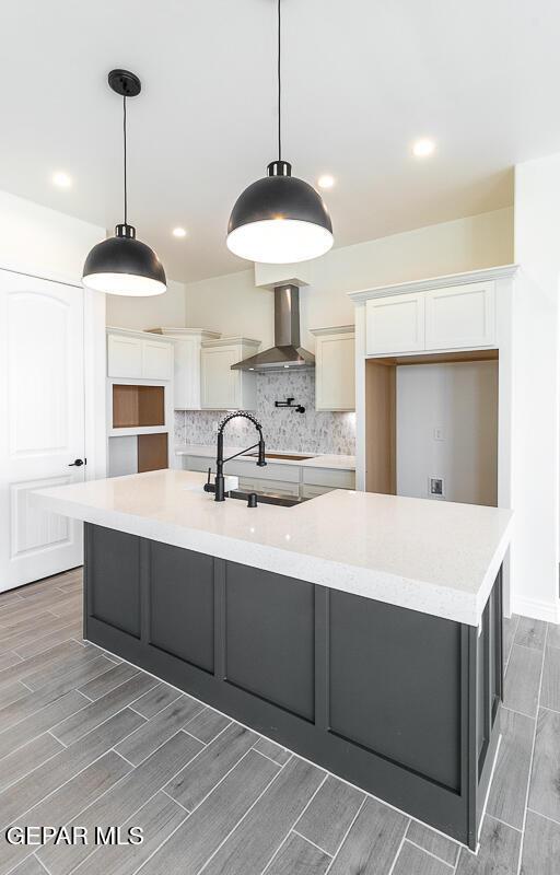 kitchen featuring a spacious island, wood tiled floor, decorative backsplash, white cabinetry, and wall chimney exhaust hood