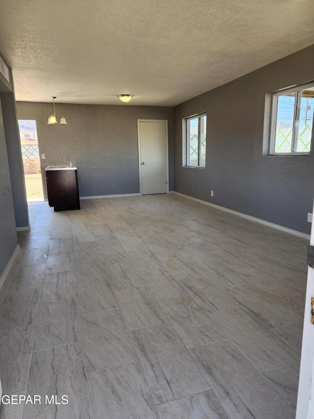 empty room featuring a wealth of natural light, a textured ceiling, and baseboards