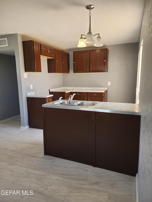 kitchen featuring visible vents, light countertops, hanging light fixtures, a textured ceiling, and a sink