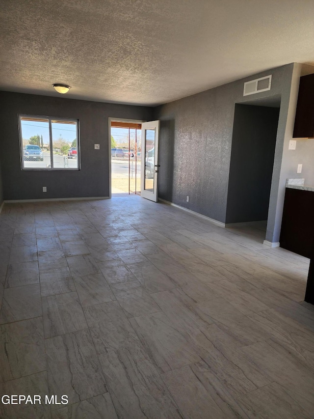 unfurnished living room with baseboards, visible vents, and a textured ceiling