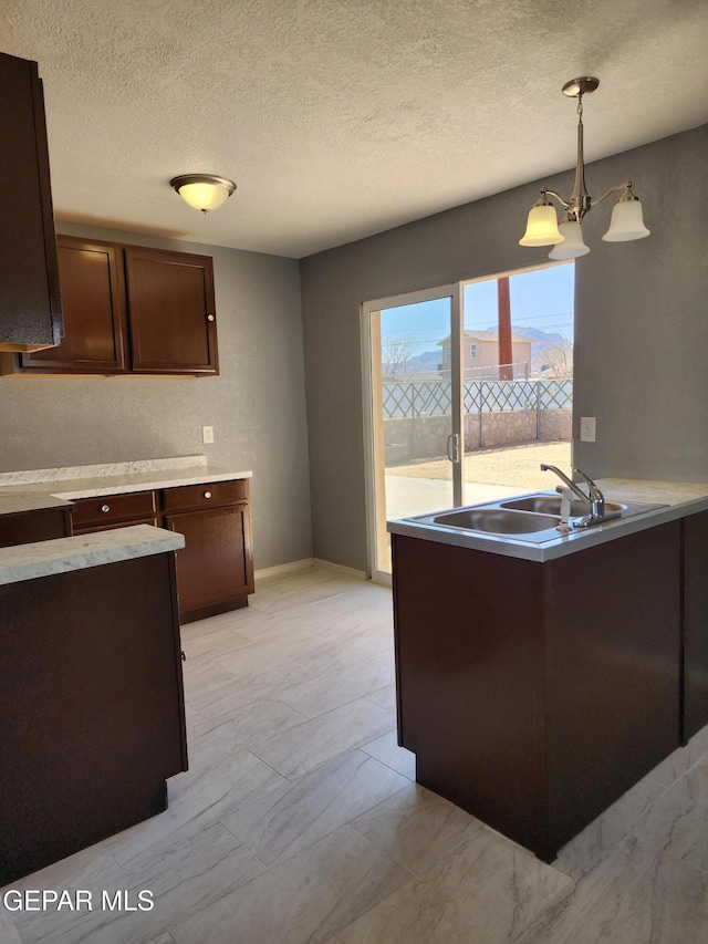 kitchen with dark brown cabinets, pendant lighting, light countertops, and a sink