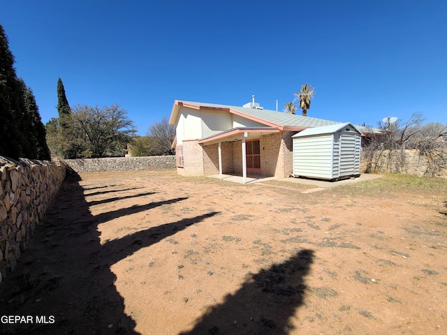 rear view of house with brick siding, fence, a storage shed, an outdoor structure, and a patio area