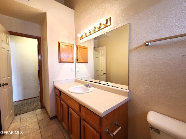 bathroom featuring vanity, toilet, a textured wall, and tile patterned flooring