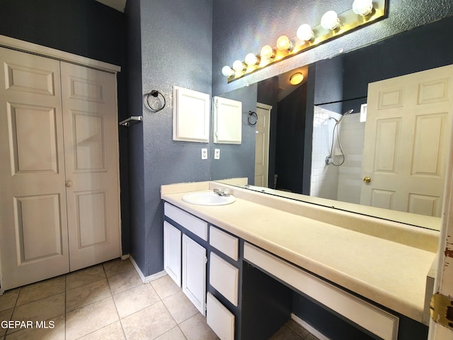 full bath featuring tile patterned floors, a tile shower, baseboards, vanity, and a textured wall