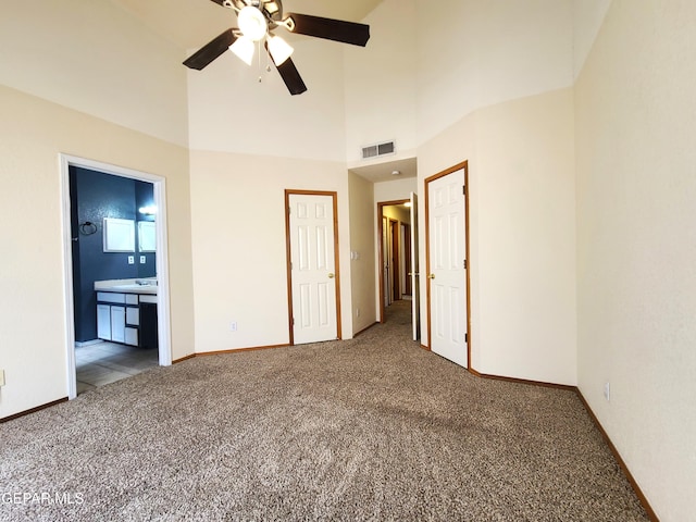 unfurnished bedroom featuring visible vents, baseboards, carpet flooring, ensuite bathroom, and a towering ceiling