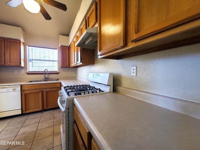 kitchen featuring brown cabinets, under cabinet range hood, a sink, white appliances, and light countertops