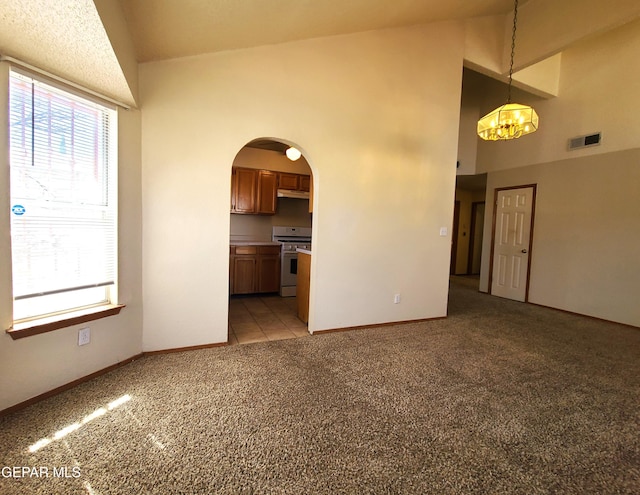 unfurnished living room featuring baseboards, visible vents, high vaulted ceiling, arched walkways, and light carpet