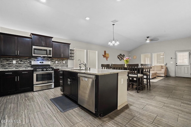 kitchen with a sink, vaulted ceiling, appliances with stainless steel finishes, tasteful backsplash, and open floor plan