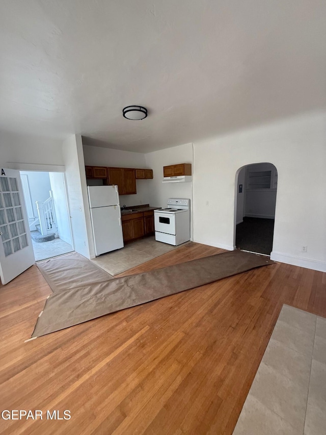 kitchen with baseboards, open floor plan, light wood-style floors, arched walkways, and white appliances