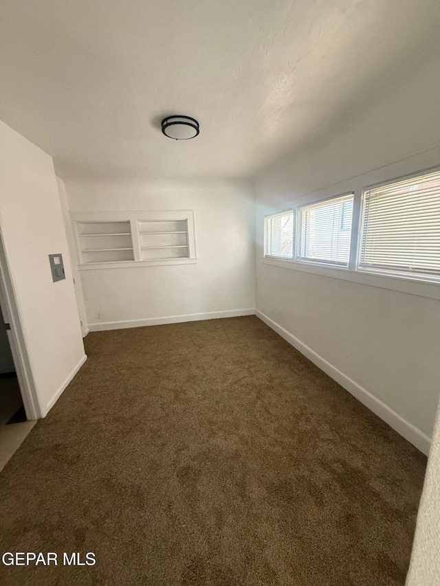 empty room featuring baseboards and dark colored carpet