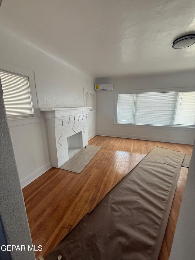 unfurnished living room featuring a fireplace, a wall mounted air conditioner, baseboards, and wood-type flooring