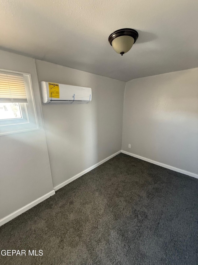 unfurnished room featuring baseboards, dark colored carpet, and a wall mounted air conditioner