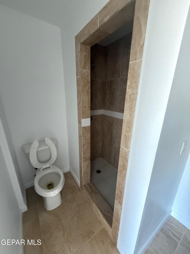 full bathroom featuring tile patterned flooring, toilet, tiled shower, and baseboards